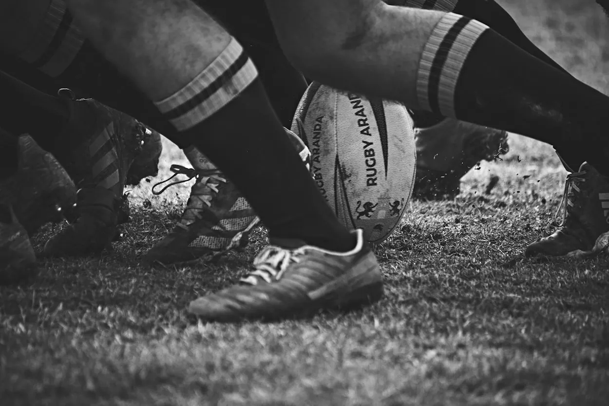 Black and white rugby photograph showing a rugby ball and players’ boots on the pitch